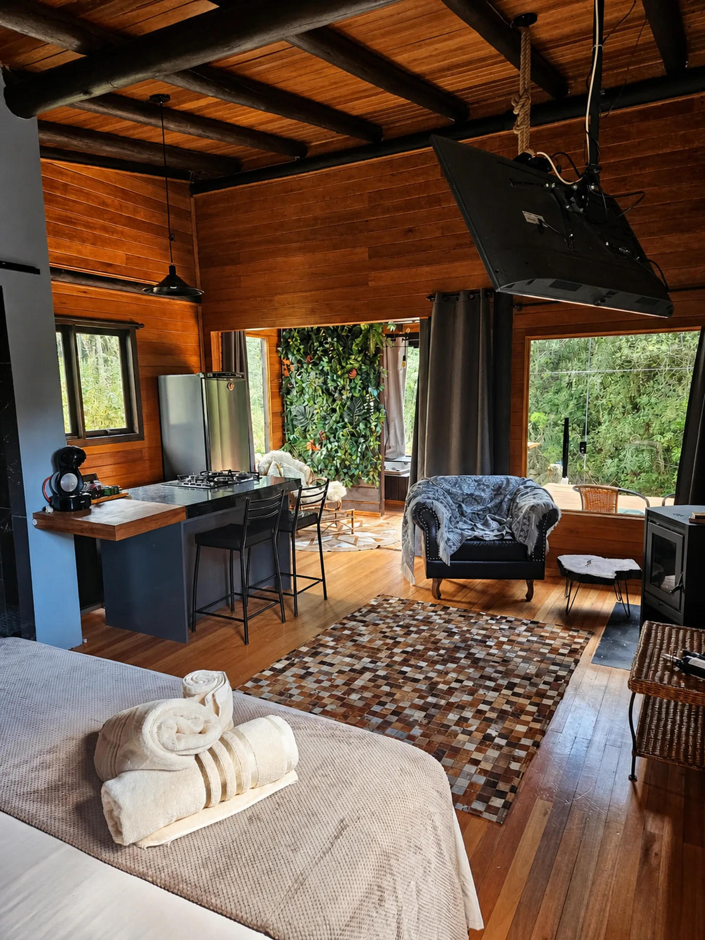 Cama, cozinha e área de estar integradas com vista para a mata na Cabana do Rio