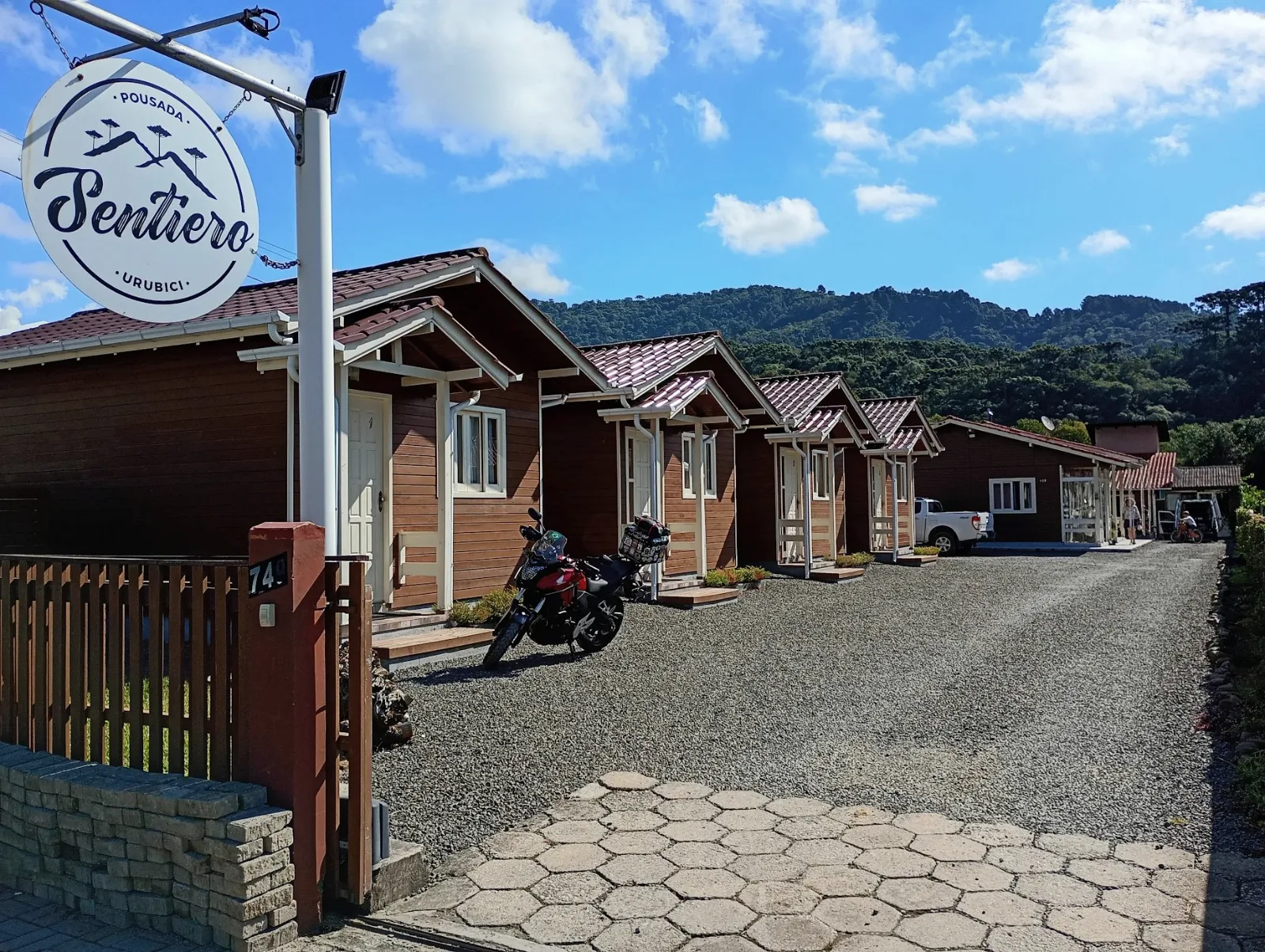 Entrada da Pousada Sentiero com placa, chalés de madeira e montanhas ao fundo