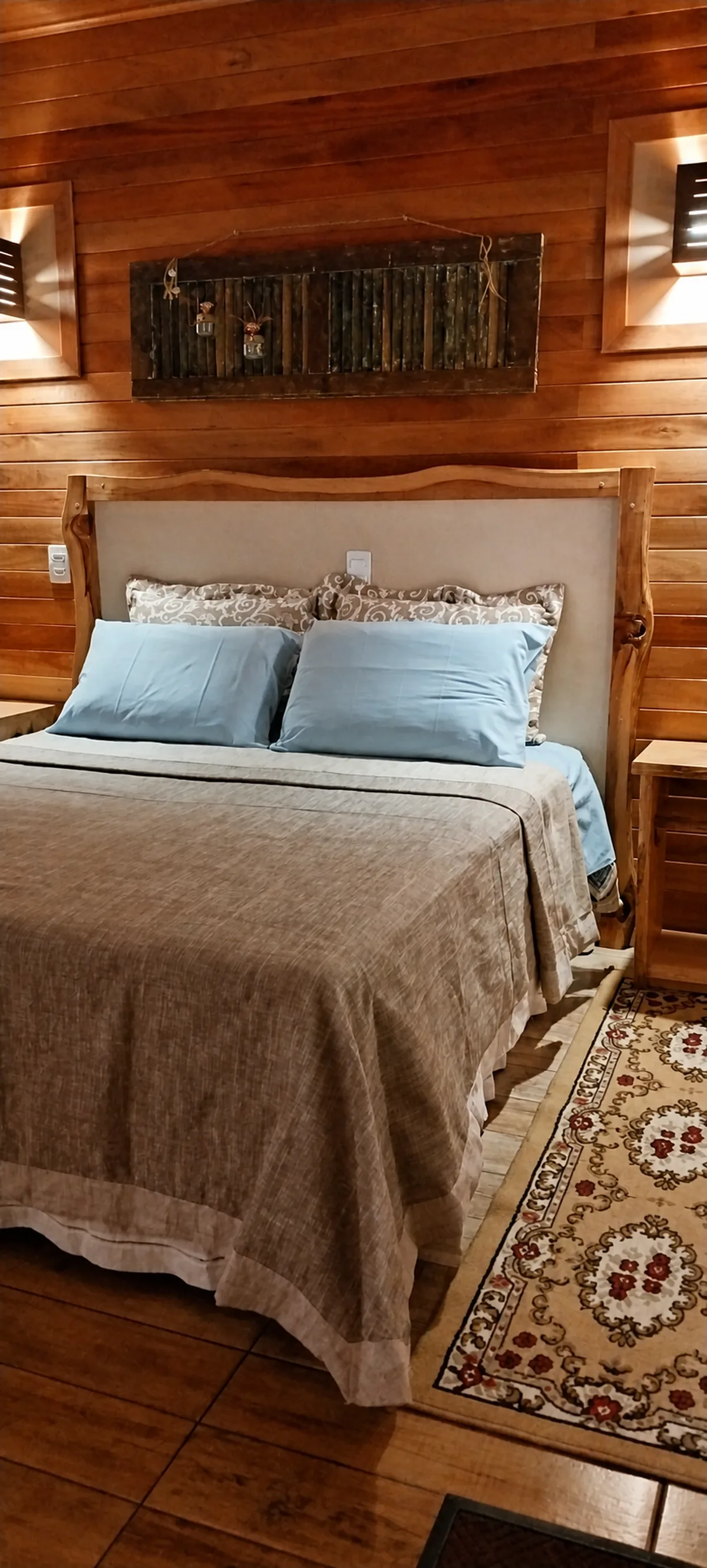 Cama de casal com travesseiros azuis em um quarto de madeira da Pousada Sentiero